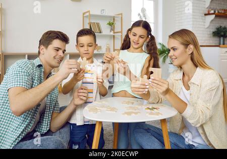 Glückliche junge Eltern und kleine Kinder verbinden Puzzle-Stücke zusammen Stockfoto