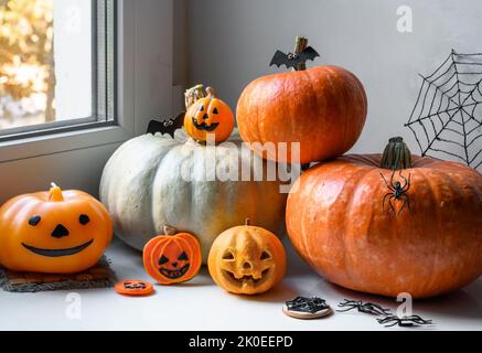 Halloween Kürbisse und Süßigkeiten auf weißem Fensterbrett zu Hause. Gemüseset und orangene Dekorationen am Fenster auf gehallten, stillem Leben. Konzept Oktober Stockfoto