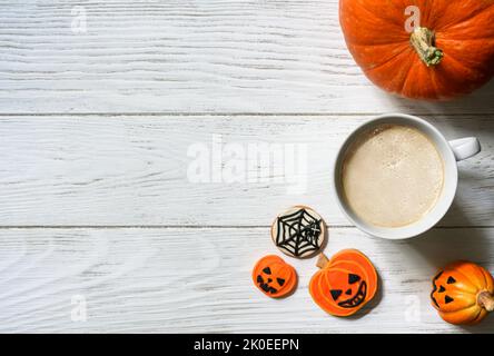 Halloween Hintergrund, Tasse Kaffee und Süßigkeiten auf Holztisch, Draufsicht. Orangefarbener Kürbis und Kekse auf weißen Holzplanken mit Platz. Party, Saison, O Stockfoto