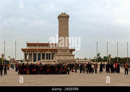 Touristen mit roten Kappen stehen vor dem zehnstöckigen Obelisken, Monument to the Peoples Heroes, mit der Chairman Mao Memorial Hall dahinter Stockfoto