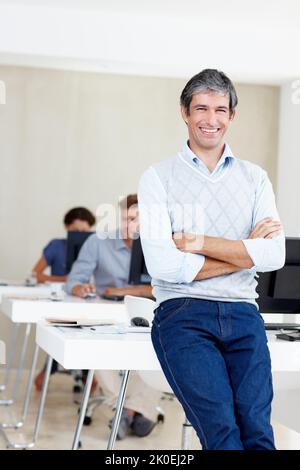 Ich bin stolz auf dieses Team. Porträt eines Büromanagers, der die Kamera anlächelt und seine Kollegen hinter ihm sitzen. Stockfoto