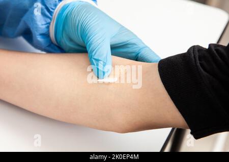 Krankenschwester, die nach der Entnahme einer Blutprobe ein Band-Aid auf den Arm eines Patienten legt Stockfoto