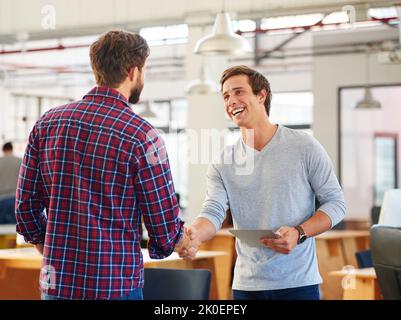 Der Beginn eines großen Geschäfts. Zwei junge Geschäftsleute, die sich in einem lässigen Büro die Hände schütteln. Stockfoto