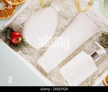 Neujahrsgeschenk. Weihnachtsschmuck mit Geschenk, weiße Schachtel mit Kosmetikprodukten und Weihnachtsschmuck auf blauem Hintergrund. Kosmetisches Modell Stockfoto