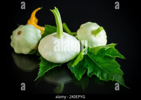 Frischer Bio-Kürbis mit Blumen und Laub isoliert auf schwarzem Hintergrund Stockfoto