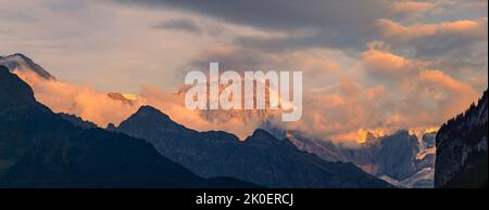 Ein breiter Panoramablick auf einen Sonnenuntergang im Berner Oberland, in der Zentralschweiz. Hier sind die beeindruckenden Berge Eiger, Mönch und Jungfrau, die p Stockfoto