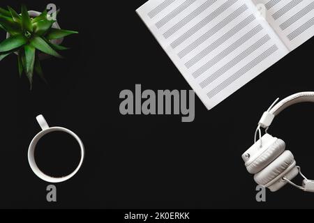 Eine Tasse Kaffee, ein Notebook und Kopfhörer auf schwarzem Hintergrund, flach liegend. Stockfoto