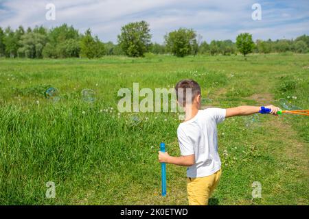 Vorschulkinder blasen an einem sonnigen Tag große Seifenblasen auf einem Feld Stockfoto