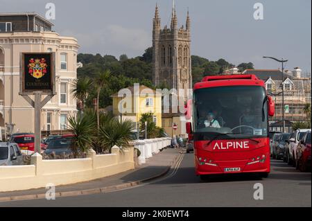 Teignmouth, Devon, England, Großbritannien. 2022. Roter Reisebus fährt durch die Küstenstadt Teignmouth im Süden von Devon, England, Großbritannien. Stockfoto
