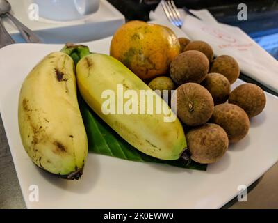 Teller mit Bananen, longanischem Obst und einer Orange in einem Hotel in Ho Chi Mihn City, Vietnam Stockfoto