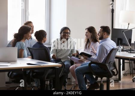 Glückliches, tausendjähriges, vielfältiges Team, das im Kreis sitzt und Teambuilding-Fähigkeiten trainiert Stockfoto
