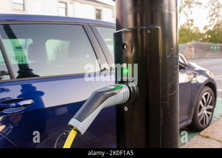 Das Elektroauto wird von einer Ladestation an einer Straßenlaterde aufgeladen. Stockfoto