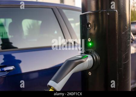 Das Elektroauto wird von einer Ladestation an einer Straßenlaterde aufgeladen. Stockfoto