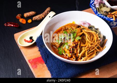 Thai Food Concept Khao Soi oder Khao Soy thai-Rind mit Eiernudeln auf Holzbrett auf schwarzem Hintergrund mit Kopierfläche Stockfoto