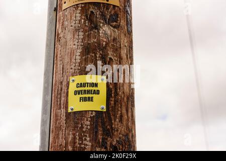 Schild an einem hölzernen Telefonmast, der die Personen darauf hinweist, dass der Mast Glasfaserkabel trägt. Stockfoto