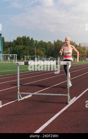 Junge Sportlerin läuft Hürden im Stadion im Freien Stockfoto