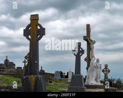 West Cork, Irland, 2. Mai 2022. Grabsteine in Form keltischer Kreuze auf einem alten katholischen Friedhof an einem bewölkten Tag, Kreuzstatue unter weißen Wolken Stockfoto