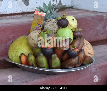 Eine hinduistische Puja-Obstschale voll mit reifen Früchten und einer Schale entfernt und dekoriert Kokosnuss und Räucherstäbchen Paket auf einer kleinen Zementbühne für den Verkauf in der Nähe Stockfoto