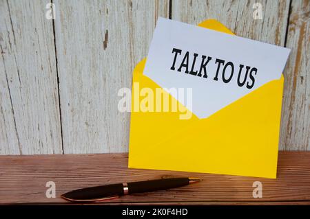 Sprechen Sie mit uns Text auf weißem Notizblock in gelbem Umschlag. Kundenservicekonzept. Stockfoto