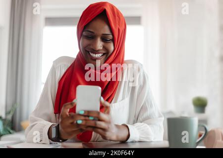 Aufgeregt afroamerikanische Frau in Hijab mit Videoanruf mit Freunden oder Liebhaber, mit modernen Smartphone zu Hause Stockfoto