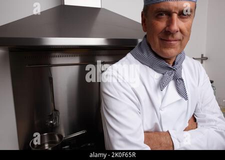 Selbstbewusster Koch mit gefalteten Händen in der Küche. Nahaufnahme Porträt eines selbstbewussten Küchenchefs mit gefalteten Händen in der Küche. Stockfoto