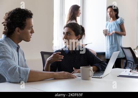 Zwei junge, multiethnische Mitarbeiter sprechen am Arbeitsplatz über das Projekt Stockfoto