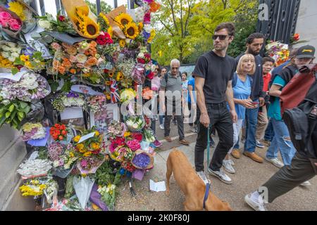 London, Großbritannien. September 2022. Eine Gruppe von Menschen versammelt sich in der Nähe einer Gedenkstätte, die mit lebhaften Blumenzutaten wie Sonnenblumen, Rosen und Lilien geschmückt ist. Die Blumensträuße werden von handgeschriebenen Notizen, Karten und einer Union Jack Flagge begleitet. Einzelne halten inne, um zu beobachten oder Respekt zu zollen, während andere vorbeigehen. Ein Hund an der Leine ist im Vordergrund sichtbar. Die Szene reflektiert kommunale Trauer und öffentliche Erinnerungen in einem urbanen Außenbereich. Im St. James Park verdanken die Menschen Königin Elizabeth Blumen. Penelope Barritt/Alamy Live News Stockfoto