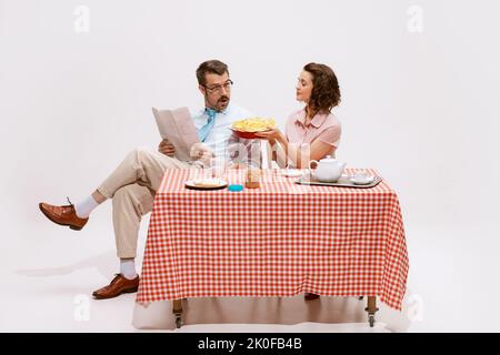 Portrait eines liebevollen Paares, das am Tisch sitzt und isoliert auf weißem Hintergrund frühstücken kann. Meine Frau gab Apfelkuchen Stockfoto