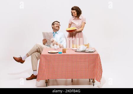 Porträt eines liebevollen Paares, eines Mannes, der Zeitung liest, einer Frau, die einen Tisch serviert, das Frühstück auf weißem Hintergrund isoliert hat. Apfelkuchen Stockfoto