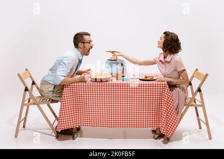 Porträt eines Paares, das am Tisch sitzt, beim Frühstück, Ehefrau, die Ehemann auf weißem Hintergrund füttert. Toast zum Frühstück Stockfoto