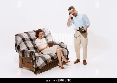 Portrait einer schönen Frau, die auf dem Sofa sitzt und Buch liest, Mann, der in der Nähe steht und telefoniert und schreit Stockfoto