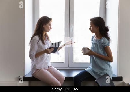 Zwei verschiedene Kollegen, Frauen, die am Bürofenster sitzen Stockfoto