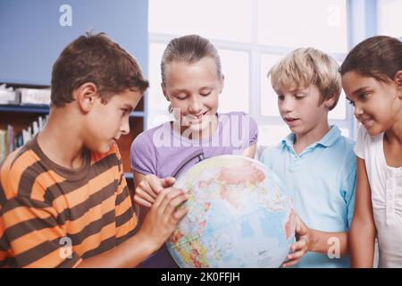 Lernen Sie die verschiedenen Länder der Welt kennen. Eine Gruppe von Schulkindern, die mit einer Erdkugel über die Welt lernen. Stockfoto