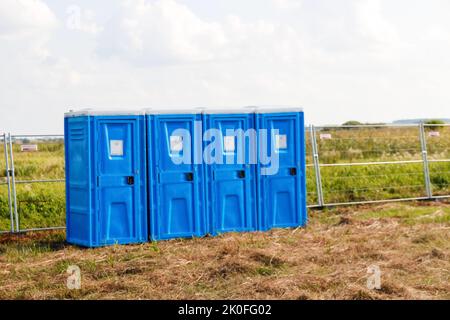 Unschärfe-Effekte von vier blauen tragbaren Bio-Toilettenkabinen auf dem Feld. Linie von chemischen Toiletten für den Urlaub, Festival und Publikum. WC. Mitarbeiter, die das tragbare Gerät verwenden Stockfoto