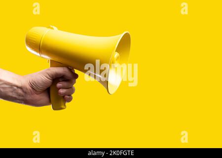 Auf einem leuchtend gelben Hintergrund ein gelbes Megaphon in der Hand einer Frau. Falsche Informationen, Gerüchte, Klatsch, gelbe Presse, Radio, Fernsehen, Wahlen deba Stockfoto