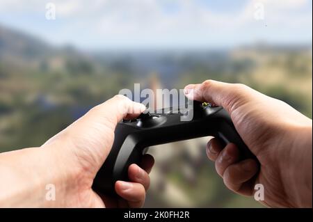 GAM22ICB Joystick in den Händen einer Person auf dem Hintergrund eines Videospiels auf dem Bildschirm. Kommunikation, Online-Spiele mit Freunden, Hobby, virtuelle r Stockfoto