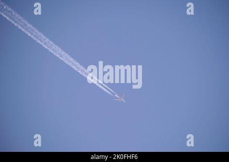 Fernes Passagierflugzeug, das auf großer Höhe am klaren blauen Himmel fliegt und weiße Rauchspuren von Kondensstreifen hinterlässt. Konzept des Luftverkehrs Stockfoto