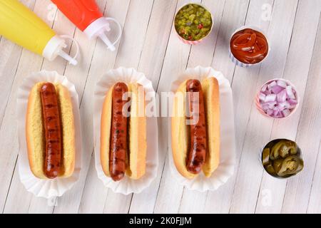 Drei gegrillte Hot Dogs, die bereit sind, auf einem rustikalen Holz-Picknicktisch garniert zu werden. High-Angle-Ansicht. Stockfoto