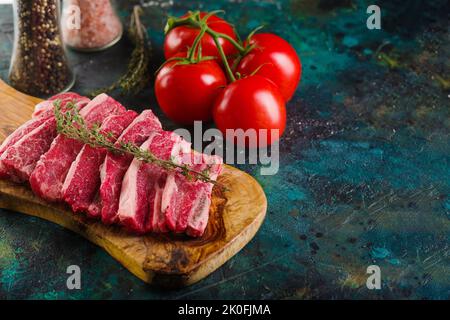 Appetitliche hausgemachte rohe Schweinesteaks, Kalb auf einem Holzschneidebrett, frische Tomaten, Gewürze, Gewürze auf dunklem Hintergrund. Rezepte zum Kochen von Fleisch Stockfoto