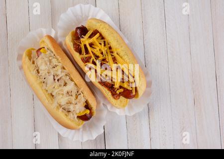 Zwei Hot Dogs, einer mit Sauerkraut und einer mit Chilischäse auf einem weißen ewood-Tisch mit Kopierfläche. Stockfoto