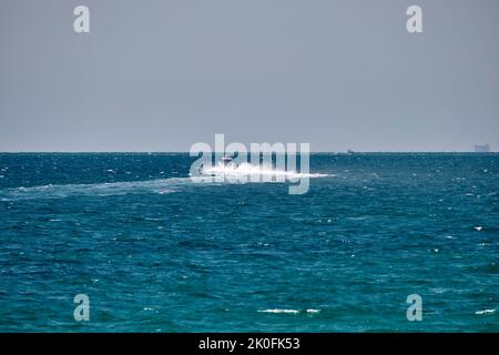 Meereslandschaft mit Wellenoberfläche aus blauem Meerwasser mit weißem Schnellboot, das schnell auf ruhigen Wellen schwimmt. Stockfoto