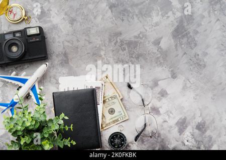 Uhren, Kamera, Pässe, Geld, Tickets und ein kleines Flugzeug auf grauem Hintergrund. Das Konzept ist Urlaub, Flugreisen, Urlaub, Geschäftsreisen. Verbot Stockfoto