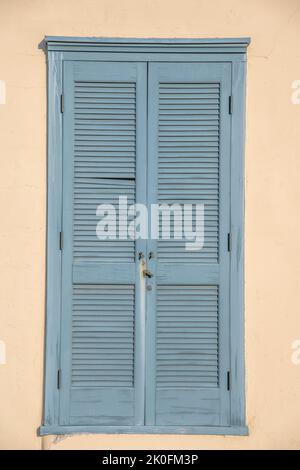 Hellblaue Fenstertür aus Holz gegen die beigefarbene Wand in der Innenstadt von Tucson, Arizona. Alte, lackierte Holztür mit Lamellen und seitlichen Scharnieren. Stockfoto