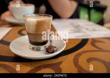 Selektiver Fokus auf Con Latte, Espresso mit Milch, serviert in einem kleinen Glas, auf einem dekorativen Tisch. Stockfoto
