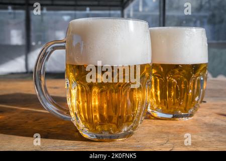 Zwei Tassen helles Bier mit Schaum auf einem Holztisch Stockfoto
