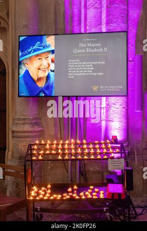 Winchester, Hampshire, Großbritannien. 11.. September 2022. Nach dem Tod von Königin Elizabeth II. Am 8.. September 2022 wurde das Innere der Winchester Cathedral in Purpur beleuchtet, mit Bildern der verstorbenen Königin, Blumen und Gebeten. Viele Menschen sind heute gekommen, um still und leise ihren Respekt zu zollen und ihre Ehrungen zu hinterlassen, indem sie ein Kondolenzbuch unterschrieben oder Kerzen angezündet haben. Das Land befindet sich bis zu seiner Beerdigung in einer Phase nationaler Trauer. Stockfoto