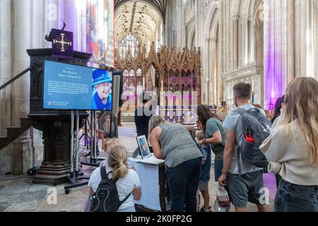 Winchester, Hampshire, Großbritannien. 11.. September 2022. Nach dem Tod von Königin Elizabeth II. Am 8.. September 2022 wurde das Innere der Winchester Cathedral in Purpur beleuchtet, mit Bildern der verstorbenen Königin, Blumen und Gebeten. Viele Menschen sind heute gekommen, um still und leise ihren Respekt zu zollen und ihre Ehrungen zu hinterlassen, indem sie ein Kondolenzbuch unterschrieben oder Kerzen angezündet haben. Das Land befindet sich bis zu seiner Beerdigung in einer Phase nationaler Trauer. Stockfoto