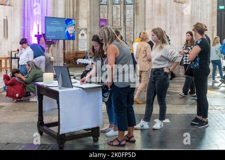 Winchester, Hampshire, Großbritannien. 11.. September 2022. Nach dem Tod von Königin Elizabeth II. Am 8.. September 2022 wurde das Innere der Winchester Cathedral in Purpur beleuchtet, mit Bildern der verstorbenen Königin, Blumen und Gebeten. Viele Menschen sind heute gekommen, um still und leise ihren Respekt zu zollen und ihre Ehrungen zu hinterlassen, indem sie ein Kondolenzbuch unterschrieben oder Kerzen angezündet haben. Das Land befindet sich bis zu seiner Beerdigung in einer Phase nationaler Trauer. Stockfoto