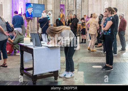 Winchester, Hampshire, Großbritannien. 11.. September 2022. Nach dem Tod von Königin Elizabeth II. Am 8.. September 2022 wurde das Innere der Winchester Cathedral in Purpur beleuchtet, mit Bildern der verstorbenen Königin, Blumen und Gebeten. Viele Menschen sind heute gekommen, um still und leise ihren Respekt zu zollen und ihre Ehrungen zu hinterlassen, indem sie ein Kondolenzbuch unterschrieben oder Kerzen angezündet haben. Das Land befindet sich bis zu seiner Beerdigung in einer Phase nationaler Trauer. Stockfoto