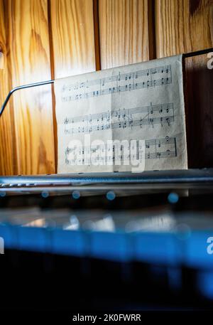Schwarz-weiße Klaviertasten gegen Noten, die auf einem Rücken hängen, sind nicht scharf. Hintergrundkonzept für Musik und Kreativität Stockfoto